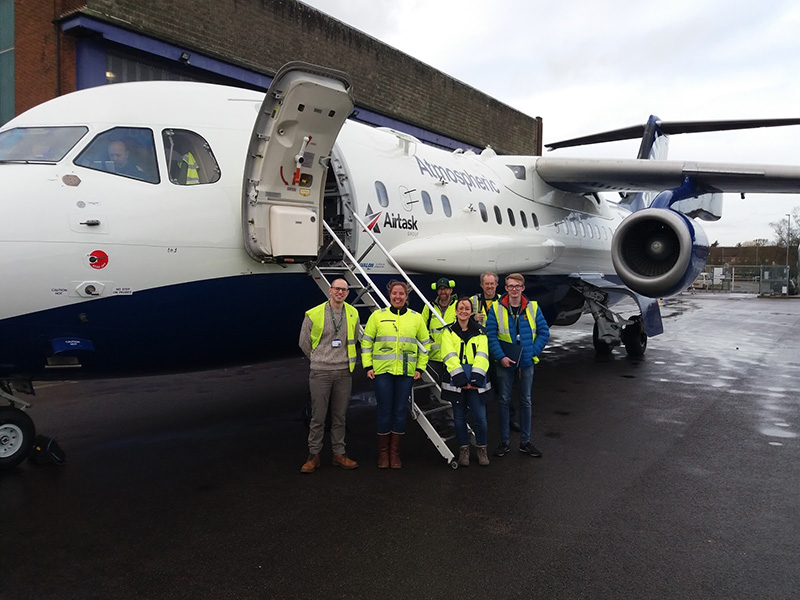 6 people wearing hi-vis jackets, stood the the FAAM research aircraft outside of the aircraft hangar