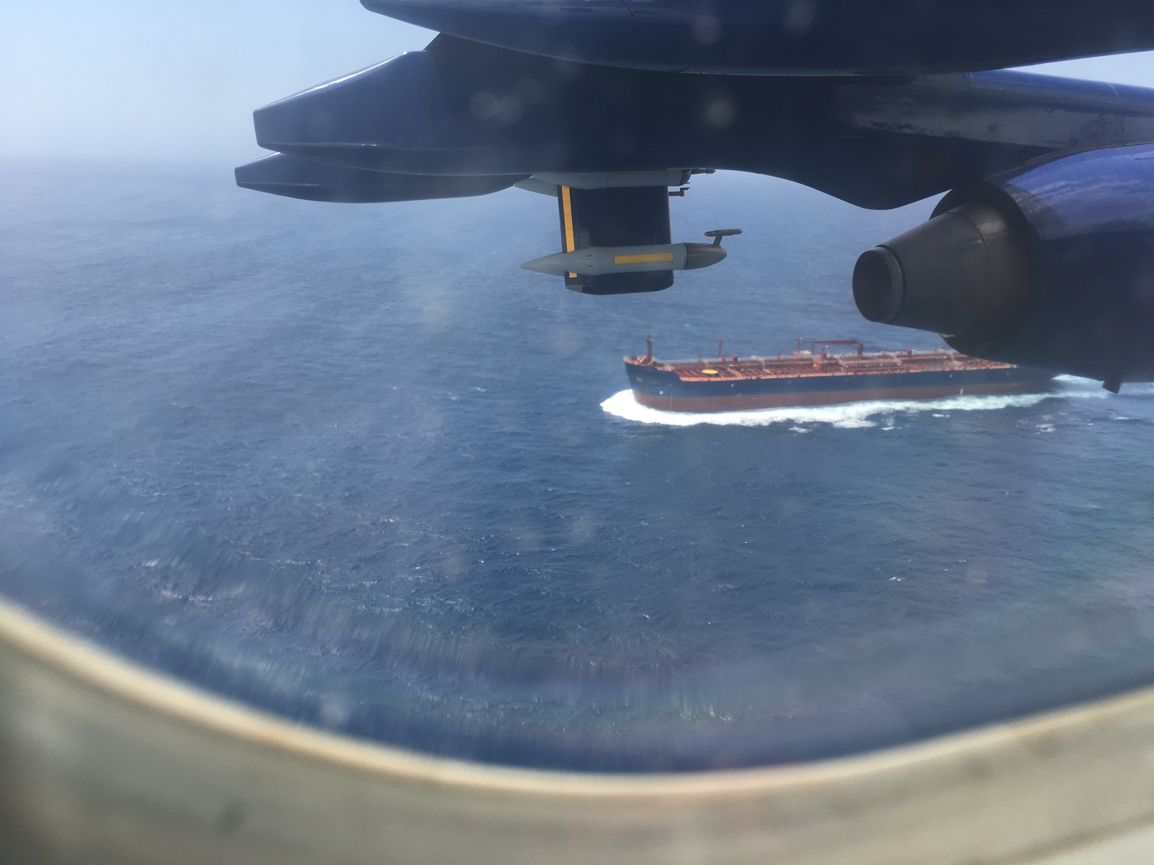 A large ship and part of a plane wing, viewed from inside an aeroplane