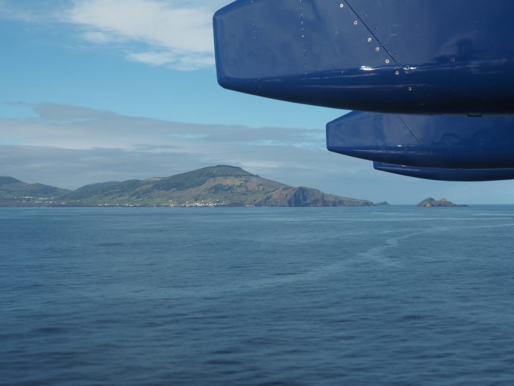 The view from an aircraft window showing part of the wing. The aircraft is flying over sea and land is visible in the distance