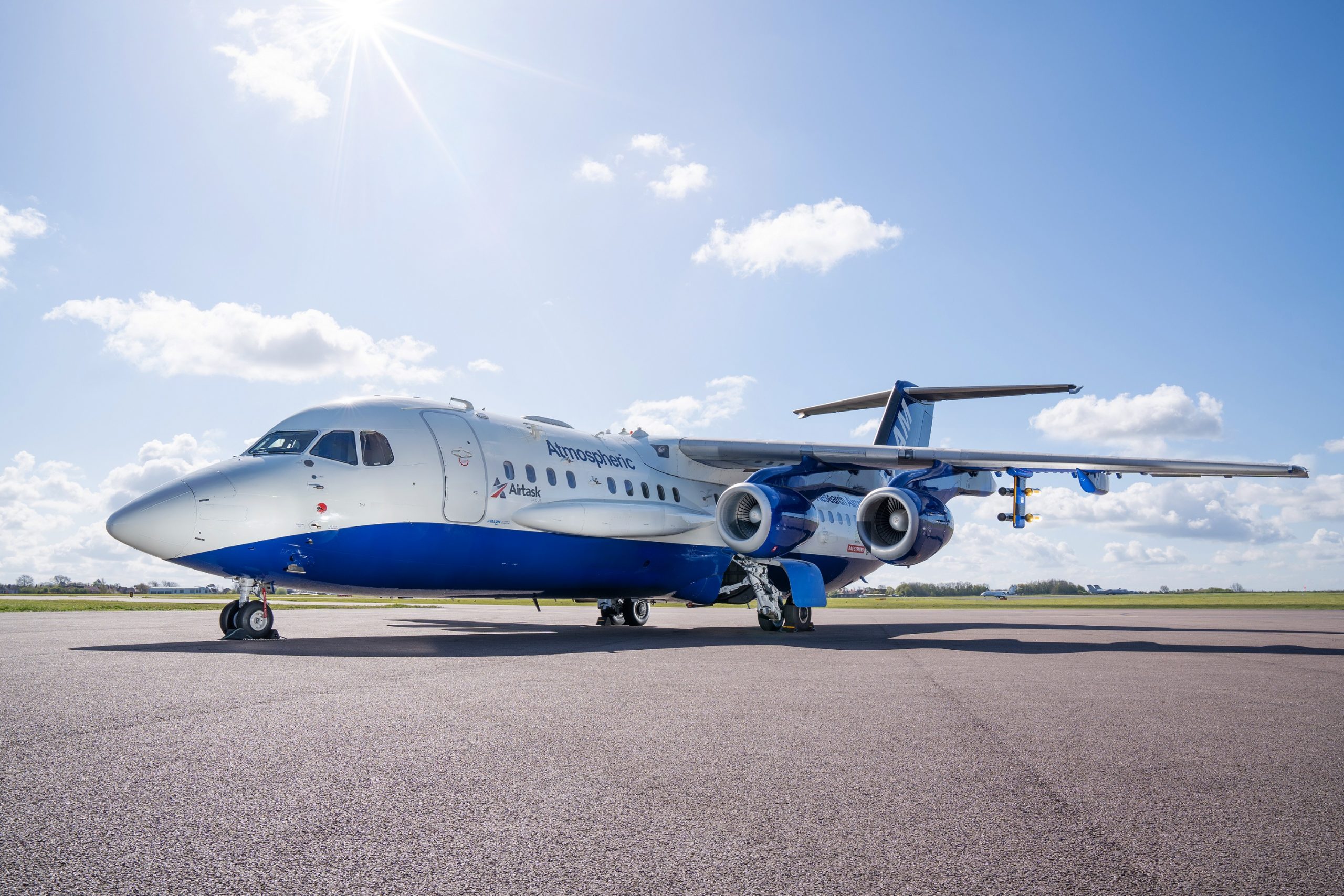 Blue and white research aircraft parked outside on apron. Green grass and blue sky with clouds in background.