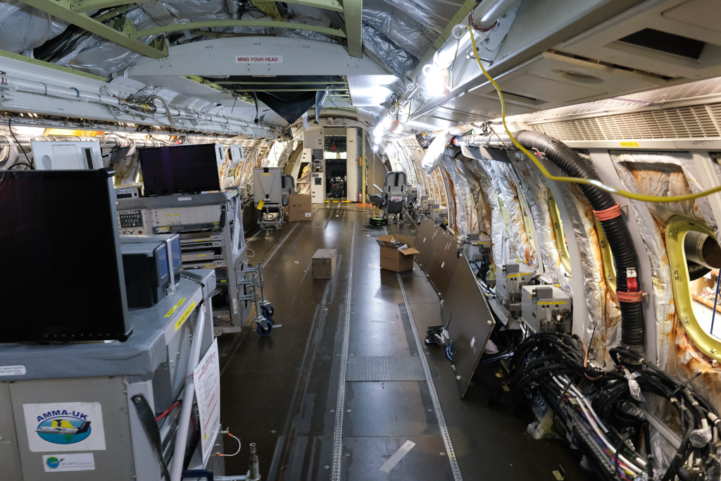 The interior of a research aircraft cabin that has been stripped out, with seats, racks and wall panels removed. Wiring, pipework and insulation is visible down the length of the cabin.