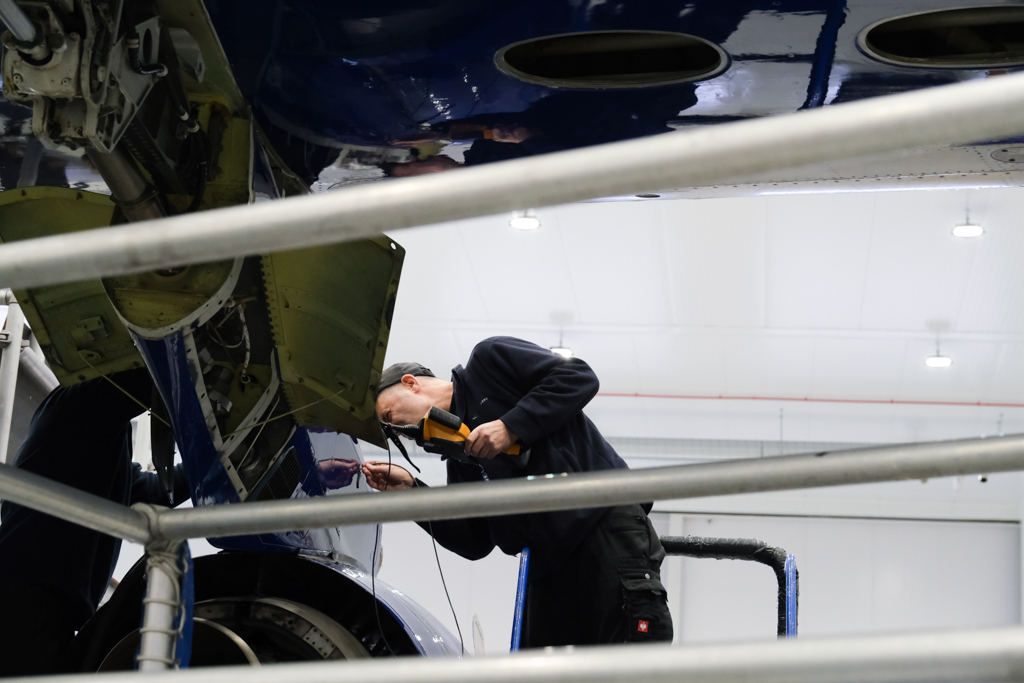 A person holding a piece of engineering equipment inspecting an engine mount on a large blue and white research aircraft.