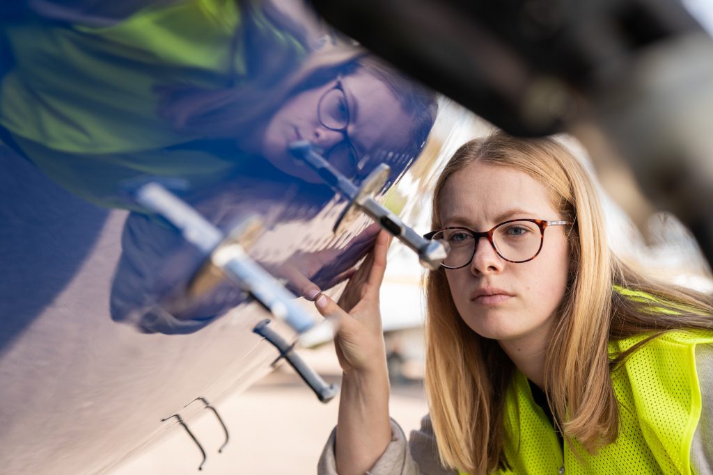 Person wearing high visibility jacket looking at external probes on blue and white research aircraft.