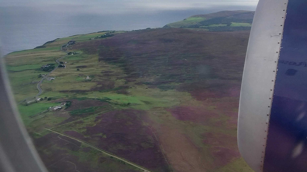 Scottish moorlands viewed from the window of a large aircraft that is flying over at low altitude. The edge of an engine is visible.