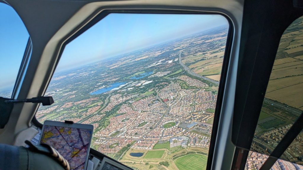 View from the cockpit window of an aircraft as it flies over a town surrounded by fields.
