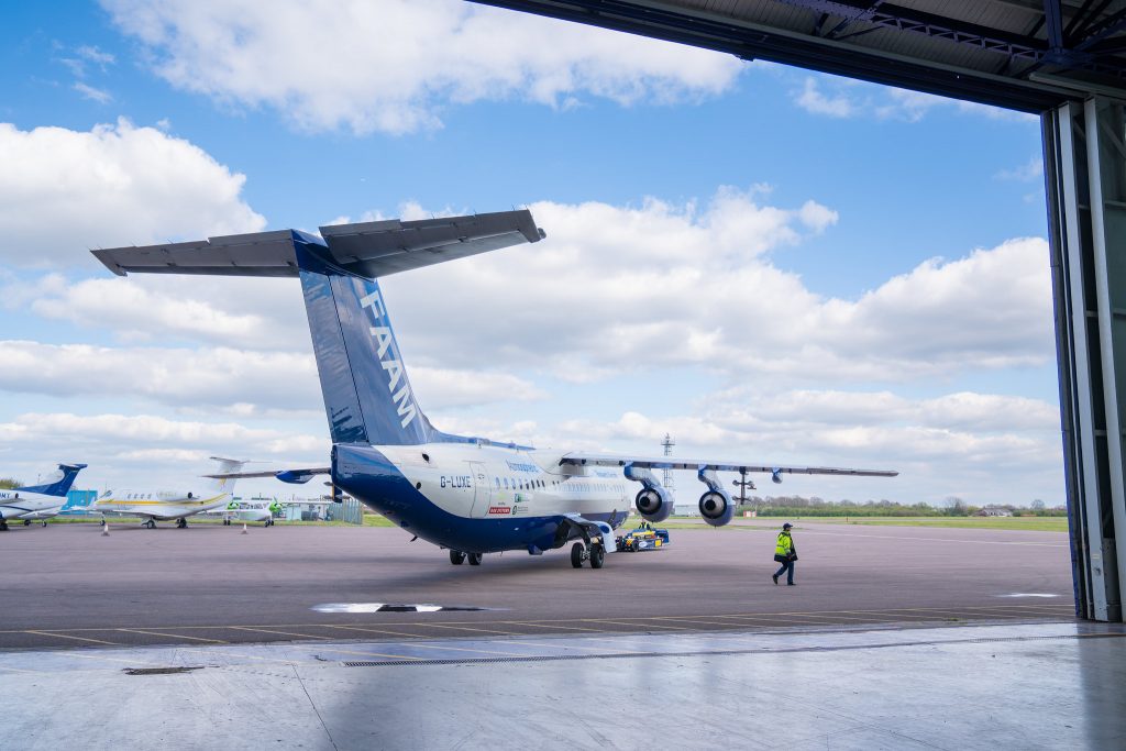 A large blue and white research aircraft being wheeled out of a hangar, accompanied by a person in hi-vis.