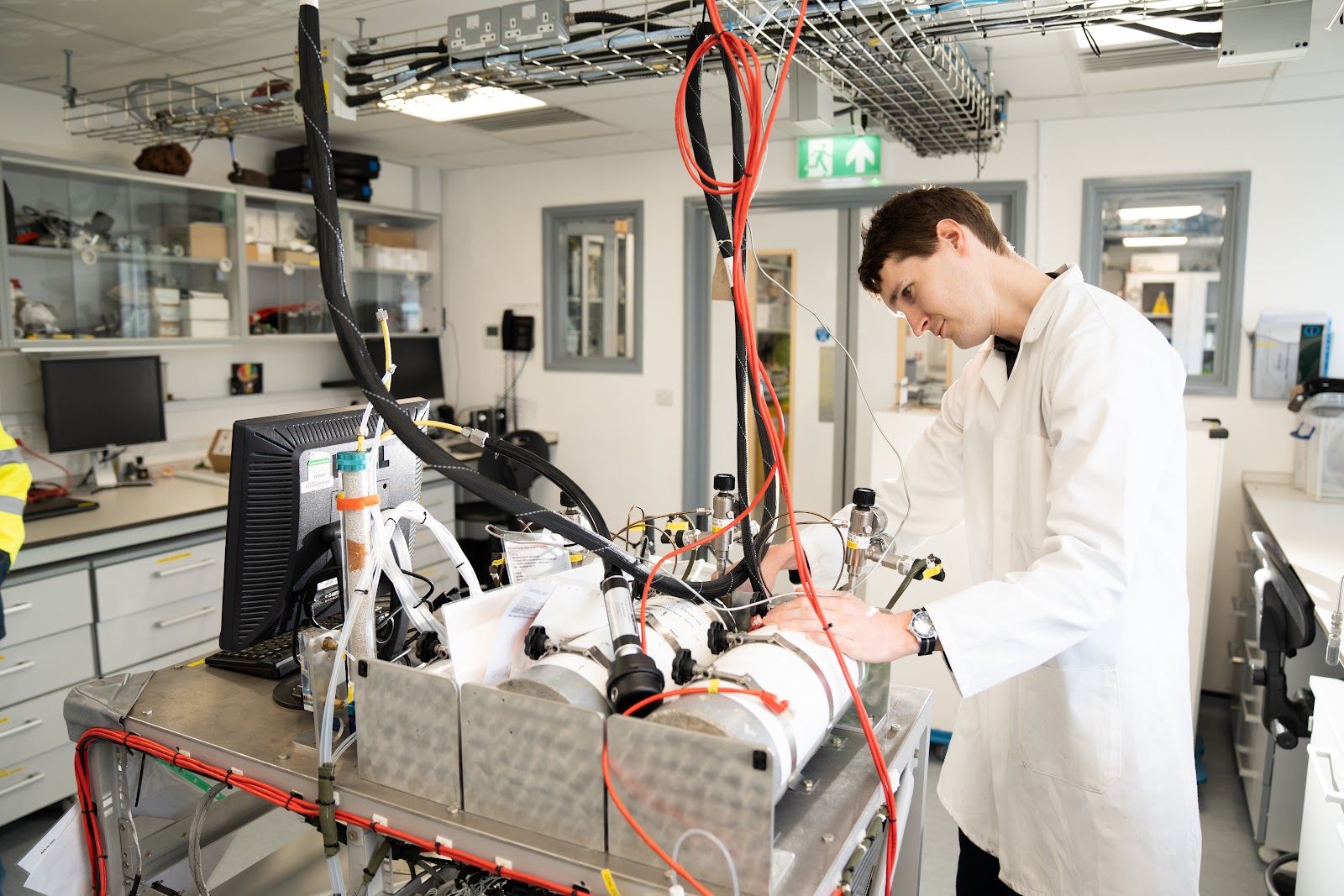 Person wearing a lab coat stood working on instrument rack inside a laboratory.
